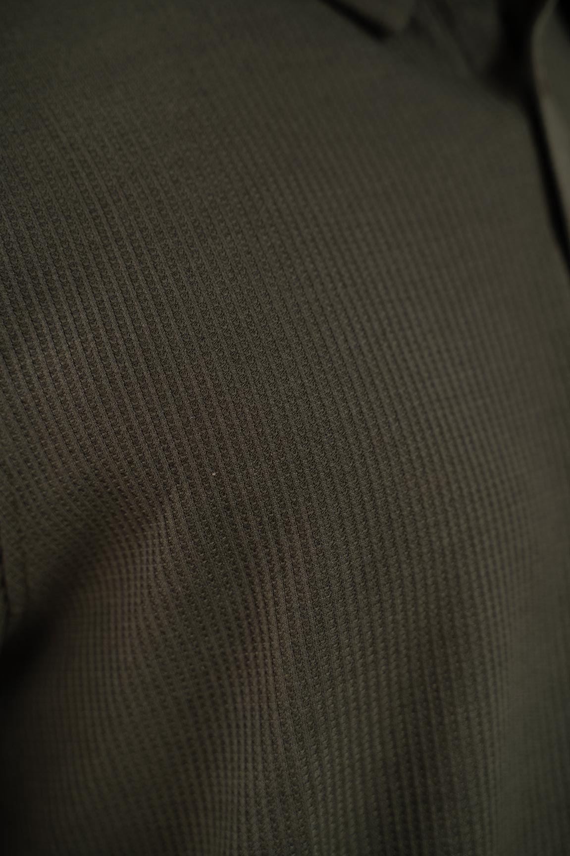 Another detailed view focusing on the hem and stitching of the olive polo shirt, highlighting its precise construction